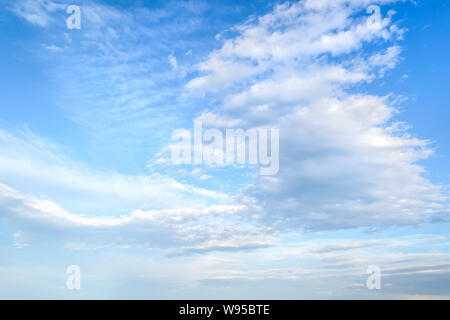 White light fluffy stratus and cirrus clouds high in the blue summer sky. Different cloud types and atmospheric phenomena. Skyscape on a sunny day. Stock Photo