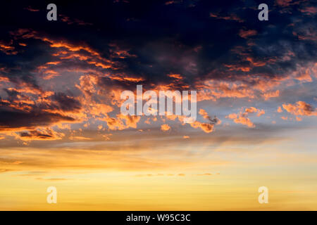 Dark thunderclouds with red orange reflections of the setting sun. Scenic storm clouds lit by the last rays of the sunset. Dramatic  skyscape. Stock Photo