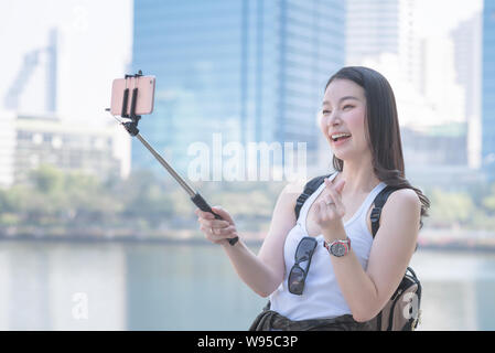 Beautiful asian woman enjoy using video call technology on a smartphone in urban city downtown. Vacation travel in summer. Stock Photo