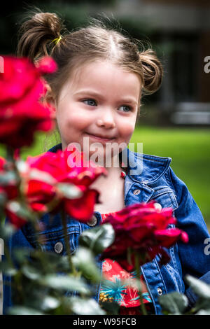 portrait of a young and adorable little girl in  a natural outdoor setting with out of focus roses Stock Photo