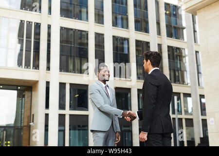 Two business partners shaking hands and greeting each other outdoors with office building in the background Stock Photo