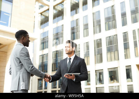 Two confident business partners in suits standing and shaking hands to each other in the city outdoors Stock Photo