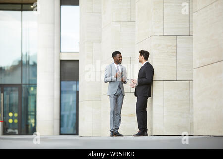 Two multiethnic coworkers standing and talking to each other they discussing working moments after meeting near the office building outdoors Stock Photo