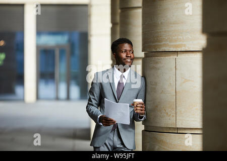 African smiling businessman in suit holding document drinking coffee and thinking about something in the city Stock Photo