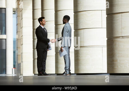 Multiethnic business people standing and shaking hands to each other before business meeting outdoors near the entrance in office building Stock Photo