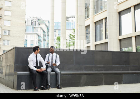 Two young businessmen discussing working moments for cup of coffee while sitting outdoors in the city Stock Photo
