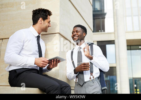 Smiling African businessman smiling and talking to his partner while he using tablet pc during break outdoors Stock Photo