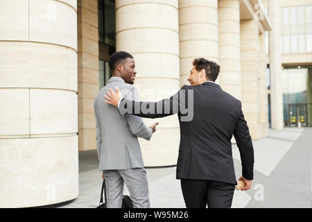 Rear view of two young businessmen meeting in the city and walking along the street together Stock Photo