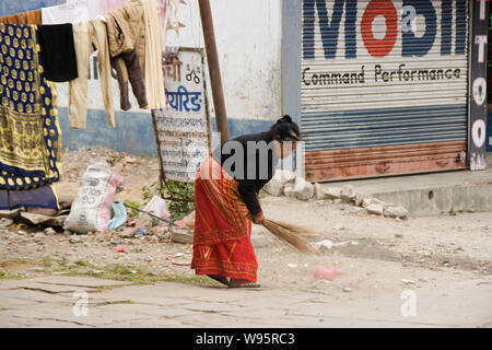 Woman in traditional dress sweeping litter on street near drying laundry, Old Bazaar area of Pokhara, Nepal Stock Photo