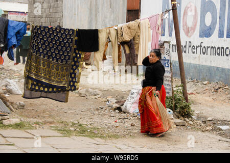 Woman in traditional dress sweeping litter on street near drying laundry, Old Bazaar area of Pokhara, Nepal Stock Photo