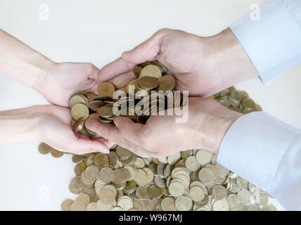 metal money in male hands giving coins to other hands, close-up against the backdrop of a pile of coins Stock Photo