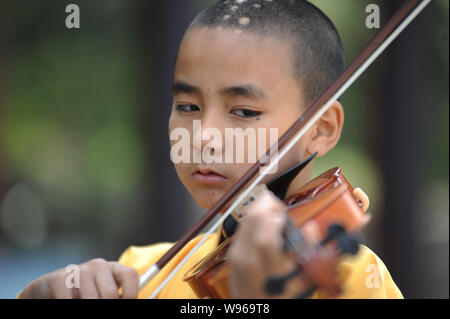 A young Chinese Buddhist monk of Guangxuan Art Troupe practices playing violin during a training session at Tiantai Temple on Tiantai Mountain in Hong Stock Photo