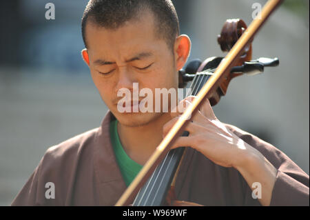 A Chinese Buddhist monk of Guangxuan Art Troupe practices playing cello during a training session at Tiantai Temple on Tiantai Mountain in HongAn coun Stock Photo