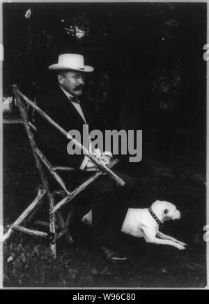 Alton Brooks Parker, 1852-1926, full length portrait, seated in rustic chair, facing right with dog on lawn wearing straw hat Stock Photo