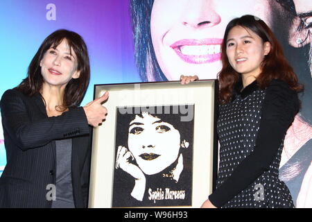 French actress Sophie Marceau, left, is presented a drawing during a press conference for the movie, Happiness Never Comes Alone, in Beijing, China, 3 Stock Photo