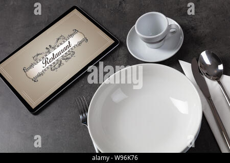 Tablet with stylish restaurant logo and laid table Stock Photo