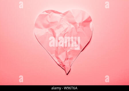 Heart symbol made from old, crumpled paper in soft pink color. Symbol of a broken heart, unhappy love. Stock Photo