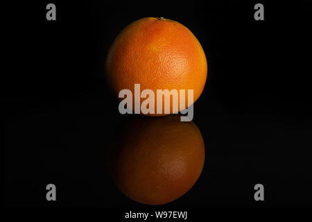 One whole fresh pink grapefruit isolated on black glass Stock Photo