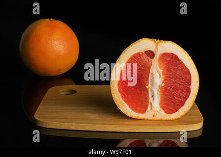 Group of one whole one half of fresh pink grapefruit on bamboo cutting board isolated on black glass Stock Photo