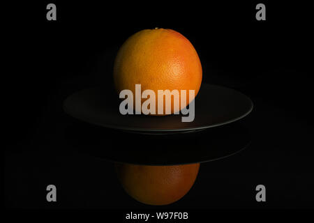 One whole fresh pink grapefruit on gray ceramic plate isolated on black glass Stock Photo