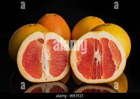 Group of four whole two halves of fresh pink grapefruit isolated on black glass Stock Photo