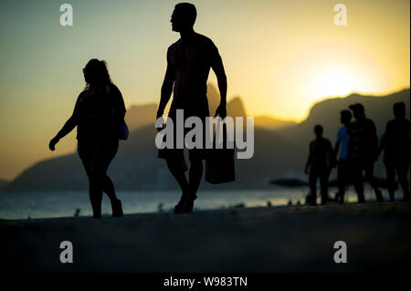 RIO DE JANEIRO - MARCH 20, 2018: People stroll along the boardwalk at the lookout point of Arpoador past a sunset silhouette of Two Brothers Mountain. Stock Photo