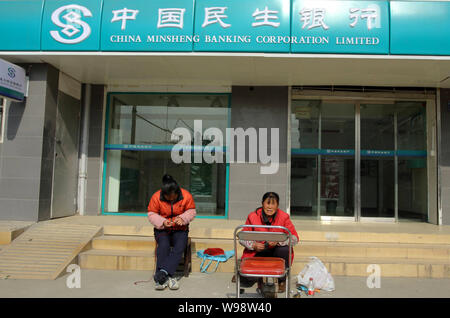 Two Chinese women sit in front of a branch of China Minsheng Banking Corporation Limited in Wuhan city, central Chinas Hubei province, 24 December 201 Stock Photo