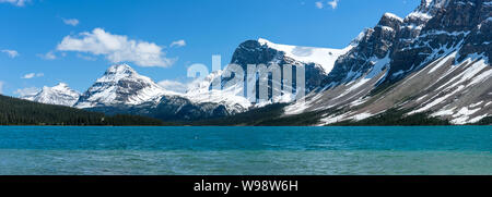 Bow Lake - A panoramic Spring view of still snow-capped mountains towering at shore of colorful Bow Lake, Banff National Park, Alberta, Canada. Stock Photo