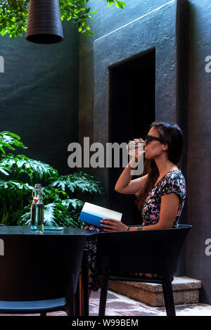Woman drinking water and reading a book on a tropical garden Stock Photo