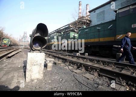 A Chinese factory worker walks past locomotives in the steel plant of Shougang Group in Shijingshan, Beijing, China, 13 January 2011.   Shougang Group Stock Photo