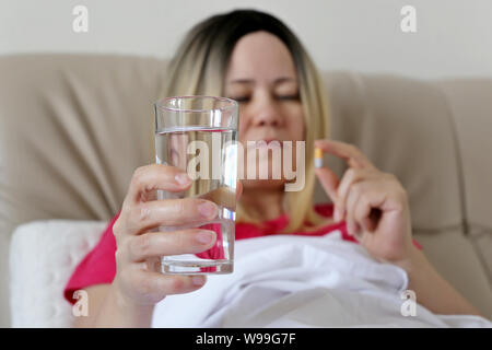 Woman taking a pill in a bed holding a water glass. Medication in capsule, concept of antibiotic, vitamin, cold and flu Stock Photo