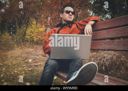 freelancer in autumn Park. Magazine editor revising new article received by email. man surfing web on a laptop connected to wifi. Student preparing Stock Photo