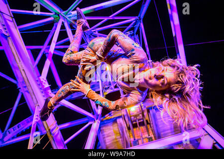 Aerial performer Rachel Fox hangs in the air from a mining pit headframe during the theatrical performance of Estah???s Story, which is set in the old mine workings at Heartlands World Heritage Site, Cornwall, featuring aerial performances, song and spoken word, retelling stories from the Cornish mining industry in the 1800s. Stock Photo