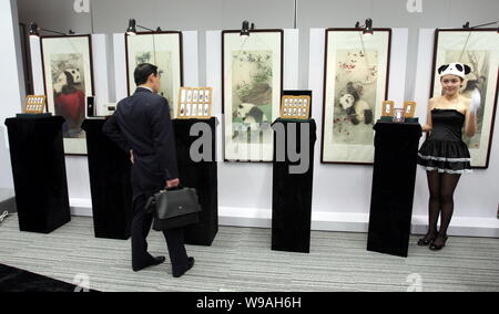 A visitor looks at panda-themed gold and silver bars for the World Expo 2010 in front of paintings of the 10 Expo pandas during a launch ceremony in S Stock Photo
