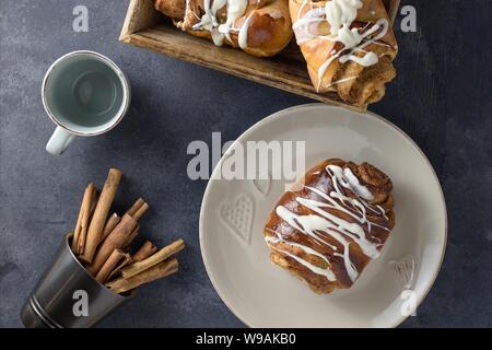 Incomplete breakfast from directly above. Delicious homemade cinnamon roll glazed with white chocolate and empty cup waiting for coffee or tea Stock Photo