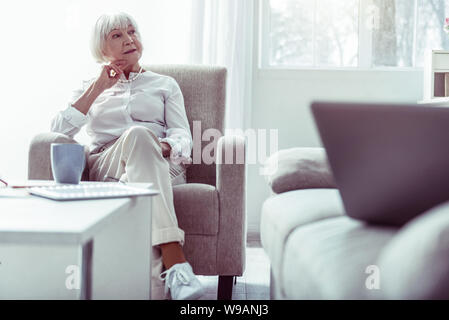 Stylish pleasant grandmother wearing white sneakers sitting in living room Stock Photo