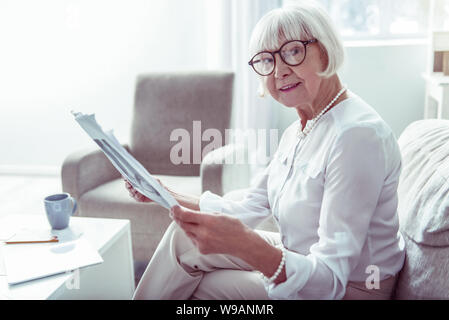 Pleasant elderly lady feeling joyful while reading local news at home Stock Photo