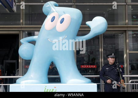 An armed Chinese policeman stands guard next to a sculpture of Haibao, the official mascot of the World Expo 2010, at the Shanghai Railway Station in Stock Photo