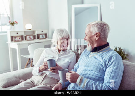 Beaming couple of pensioners feeling happy enjoying tea time together Stock Photo