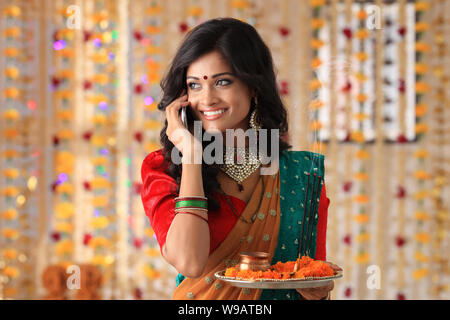 Young woman holding puja thali and talking on mobile phone Stock Photo