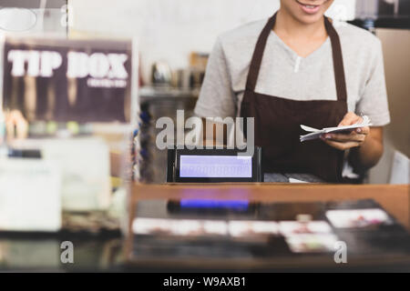 Female cashier operating cash register with order in her hand in cafe. Stock Photo