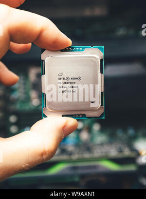 Paris, France - May 31, 2019: Front view of engineer male hand holding new professional Intel Xeon E5-2687w v4 CPU processor with Dell Precision Workstation in the background - vertical image Stock Photo