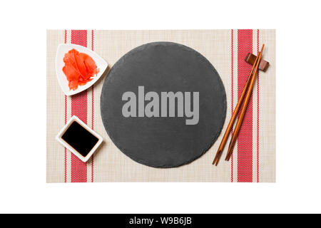 Emptyround black slate plate with chopsticks for sushi and soy sauce, ginger on sushi mat background. Top view with copy space for you design. Stock Photo