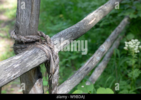 Knot bound wooden stick fence on a background of green grass. rope tied of old fence.  close up Stock Photo