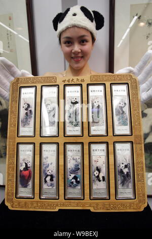 A Chinese showgirl displays a set of 10 panda-themed silver bars for the World Expo 2010 in front of paintings of the 10 Expo pandas during a launch c Stock Photo