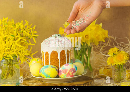 Table decorating for Easter holiday.  Easter eggs and Easter decoration on the wooden background. Female hand with sugar powder for cake. Easter cake Stock Photo
