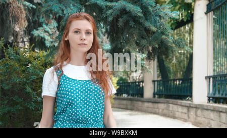 Smiling beautiful red-haired woman outdoor. Freckled ginger girl walks in green spring park. Cute redhead teenager with copy space.