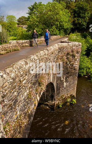 UK, England, Devon, Staverton, two male walkers crossing old stone bridge over River Dart Stock Photo