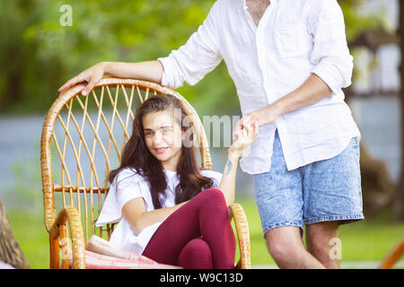Happy couple at barbecue dinner on sunset time. Having meal together outdoor in a forest glade. Look happy together. Celebrating and relaxing. Summer lifestyle, food, family, relation concept. Stock Photo