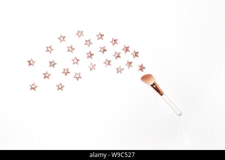 Make up brush on a pastel pink background with gold glitter stars. Flat lay top view copy space. Stock Photo